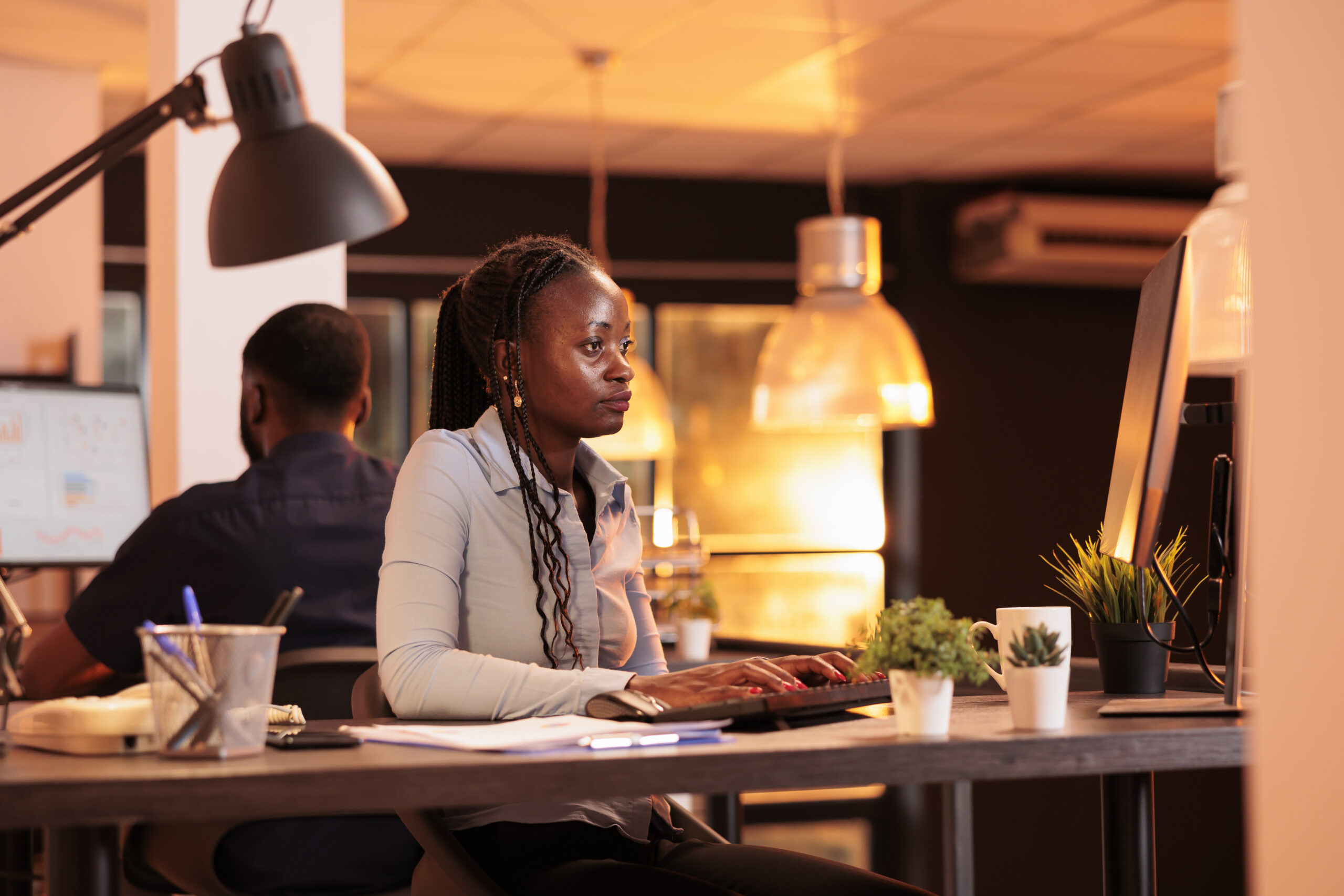 African american woman doing startup project work on computer, using research information to create business report on email. Looking at online paperwork on pc monitor during sunset.